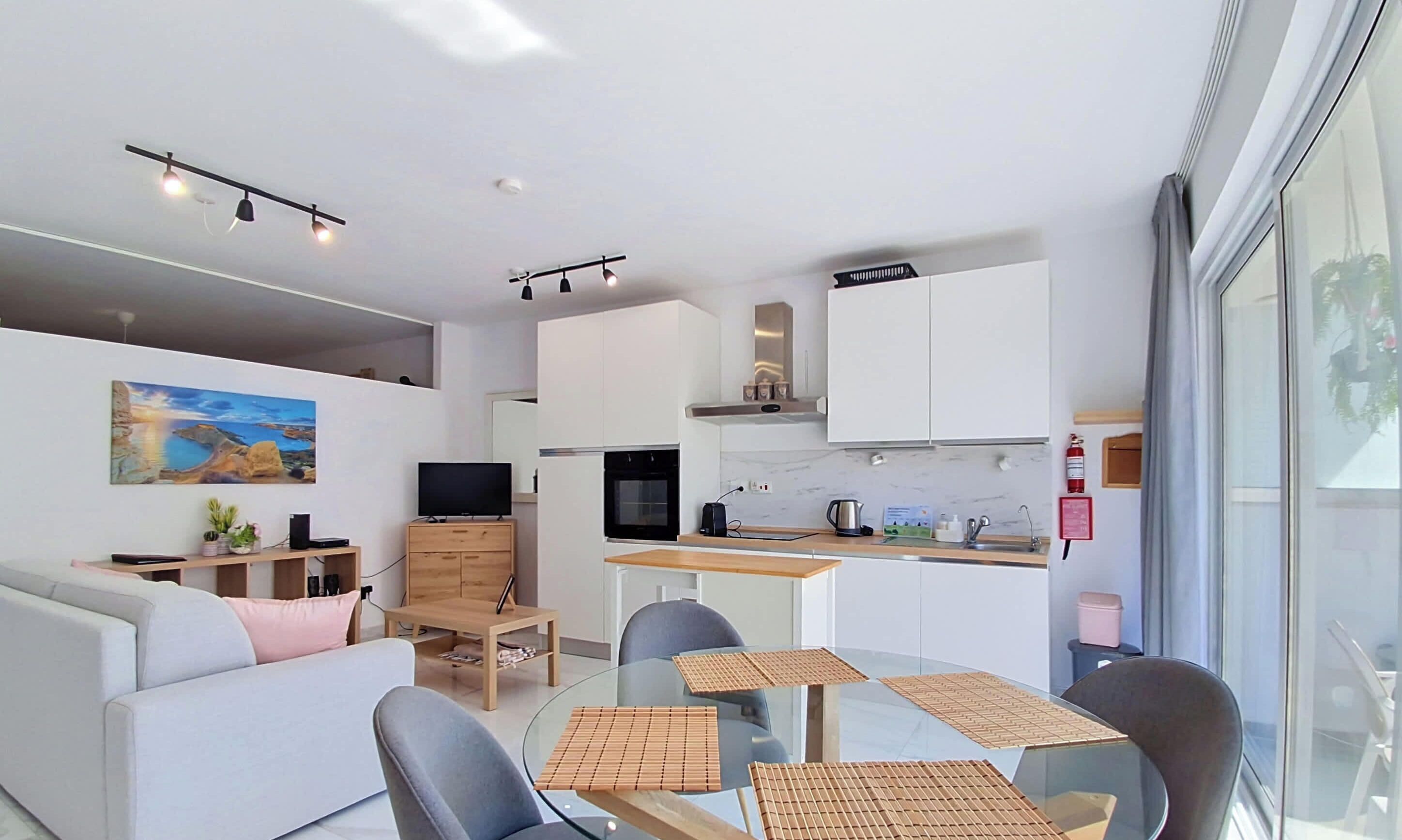 A modern living space with a sofa, a dining table with chairs, a kitchen area, and a painting on the wall.