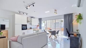 A modern living room with a sofa, a dining area with chairs, a kitchen with cabinets, and a balcony with a view.