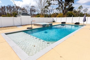 Ein rechteckiger Pool mit einer gefliesten Kante, umgeben von einem weißen Zaun, mit blauem Himmel im Hintergrund.