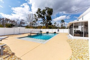 A backyard with a swimming pool, a covered patio, and a white fence.