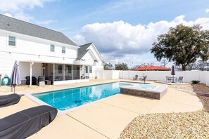 A backyard with a swimming pool, a covered patio, and a tree.