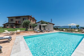 A pool area with lounge chairs and umbrellas, a stone building with a garden, and a clear sky. - Tenuta Orsini 9+3, Emma Villas (Castiglione in Teverina)