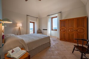 A bedroom with a bed, bedside lamps, a chair, a wooden wardrobe, and a window with curtains. - Tenuta Orsini 9+3, Emma Villas (Castiglione in Teverina)