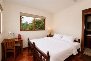 A bedroom with a wooden bed, a desk, a chair, a window with a view of trees, and a television on a wooden cabinet.