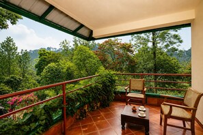 A balcony with a view of lush greenery and hills. There are two wicker chairs and a small table with a cup and saucer. - Canopy Hills Resort Munnar (Munnar)