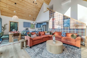 A modern living room with a large sectional sofa, a coffee table, and a dining area with chairs and a table. - Close to Sunday River: Hot Tub, Sauna, Cold Plunge (Bethel)
