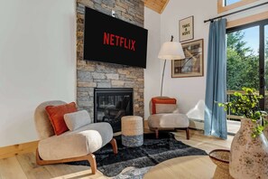 Ein Wohnzimmer mit Kamin aus Stein, einem darüber montierten Flachbildfernseher und einer gemütlichen Sitzecke mit zwei Sesseln und einem Beistelltisch.