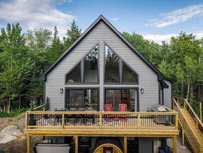 A modern house with a large deck, a staircase, and a view of the surrounding forest. - Close to Sunday River: Hot Tub, Sauna, Cold Plunge (Bethel)