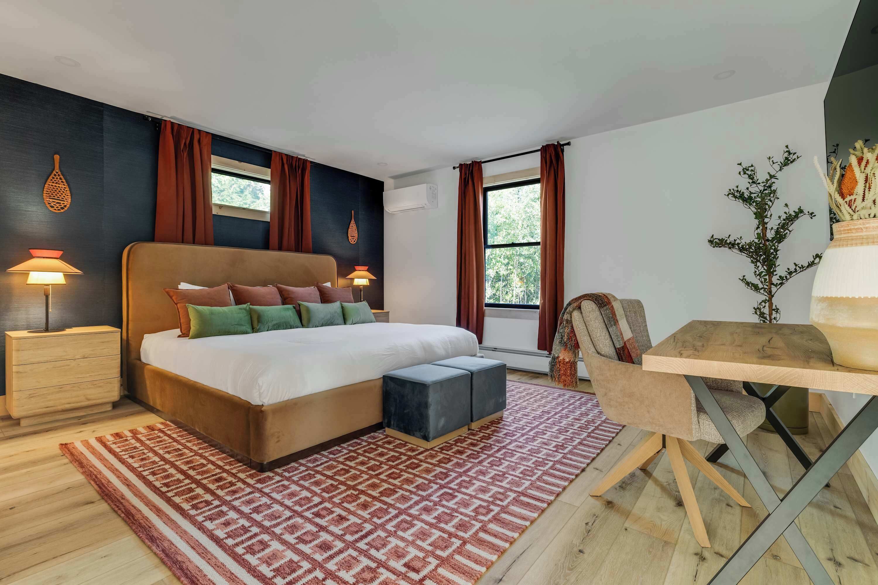 A modern bedroom with a large bed, bedside tables, a desk, and a view of greenery outside.
