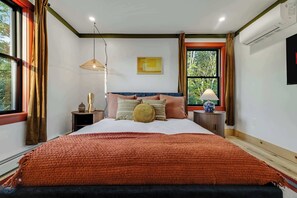 Ein Schlafzimmer mit einem großen Bett, einem Nachttisch, einer Lampe, einem Fenster mit Vorhängen und einer Wand-Klimaanlage.