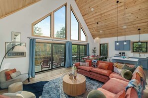 A spacious living area with a large window, a cozy seating area, and a kitchen with blue cabinets. - Close to Sunday River: Hot Tub, Sauna, Cold Plunge (Bethel)