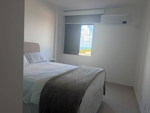 A bedroom with a bed, a window with a view, and an air conditioning unit. - Ocean View Ponta Verde (Maceió)
