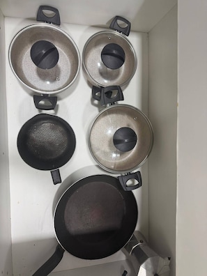 A kitchen with four pots and pans, two frying pans, and two saucepans. - Ocean View Ponta Verde (Maceió)