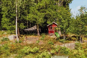Eine rote Holzhütte, umgeben von dichtem Wald, mit einer Hängematte und einem grünen Stuhl.