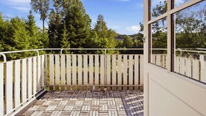 Ein Balkon mit Holzboden und weißer Brüstung, der auf einen bewaldeten Bereich blickt.