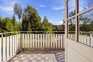 Ein Balkon mit Holzboden und weißer Brüstung, der auf einen bewaldeten Bereich blickt.