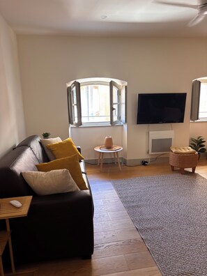A living room with a sofa, a television, a small table, and a window. - The Duplex de l'Équerre – Charm & Comfort in the Heart of Toulon (Toulon)