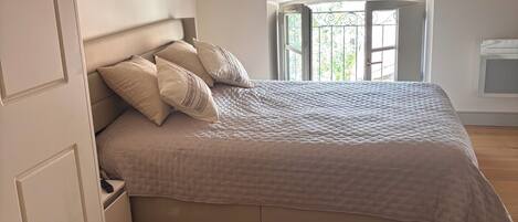 Un dormitorio con cama, mesita de noche, armario, ventana con vistas y puerta.