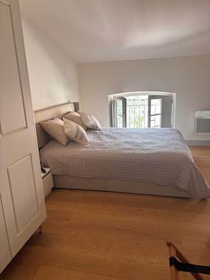 Ein Schlafzimmer mit einem Bett, einem Nachttisch, einem Kleiderschrank, einem Fenster mit Aussicht und einer Tür.