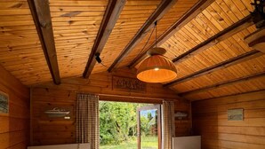 A cabin with two single beds, a wooden ceiling, and a view of greenery outside.