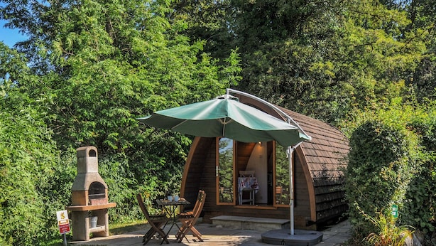 A rustic outdoor seating area with a brick oven, wooden chairs, and a table under a green umbrella. - Yar Tor (Tavistock)