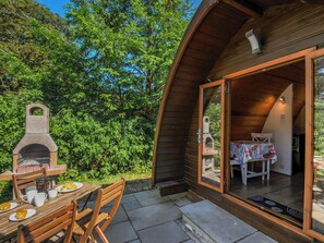 A wooden outdoor dining area with a stone pizza oven, a table with a tablecloth, and a view of the surrounding greenery. - Yar Tor (Tavistock)