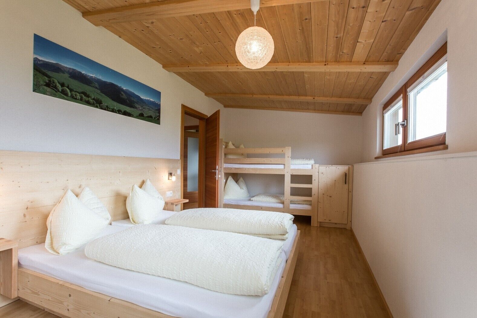 A bedroom with a bunk bed, a wooden ceiling, a bedside lamp, and a window.