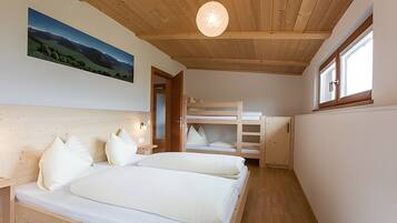 Een slaapkamer met twee bedden, een stapelbed, houten plafond en een schilderij van een landschap.