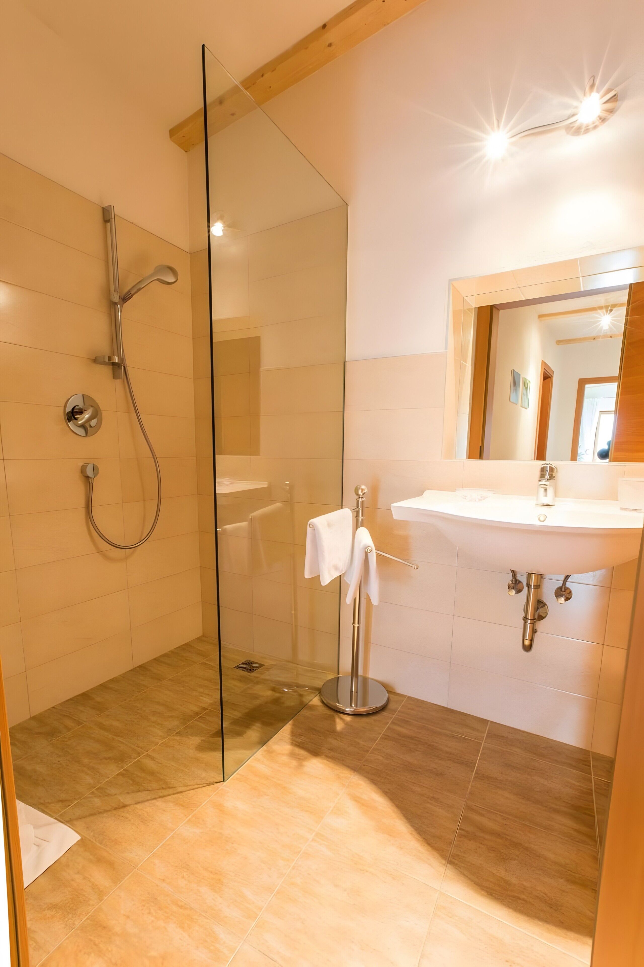 Ein modernes Badezimmer mit Duschkabine aus Glas, einem weißen Waschbecken und einer Holzbalkendecke.