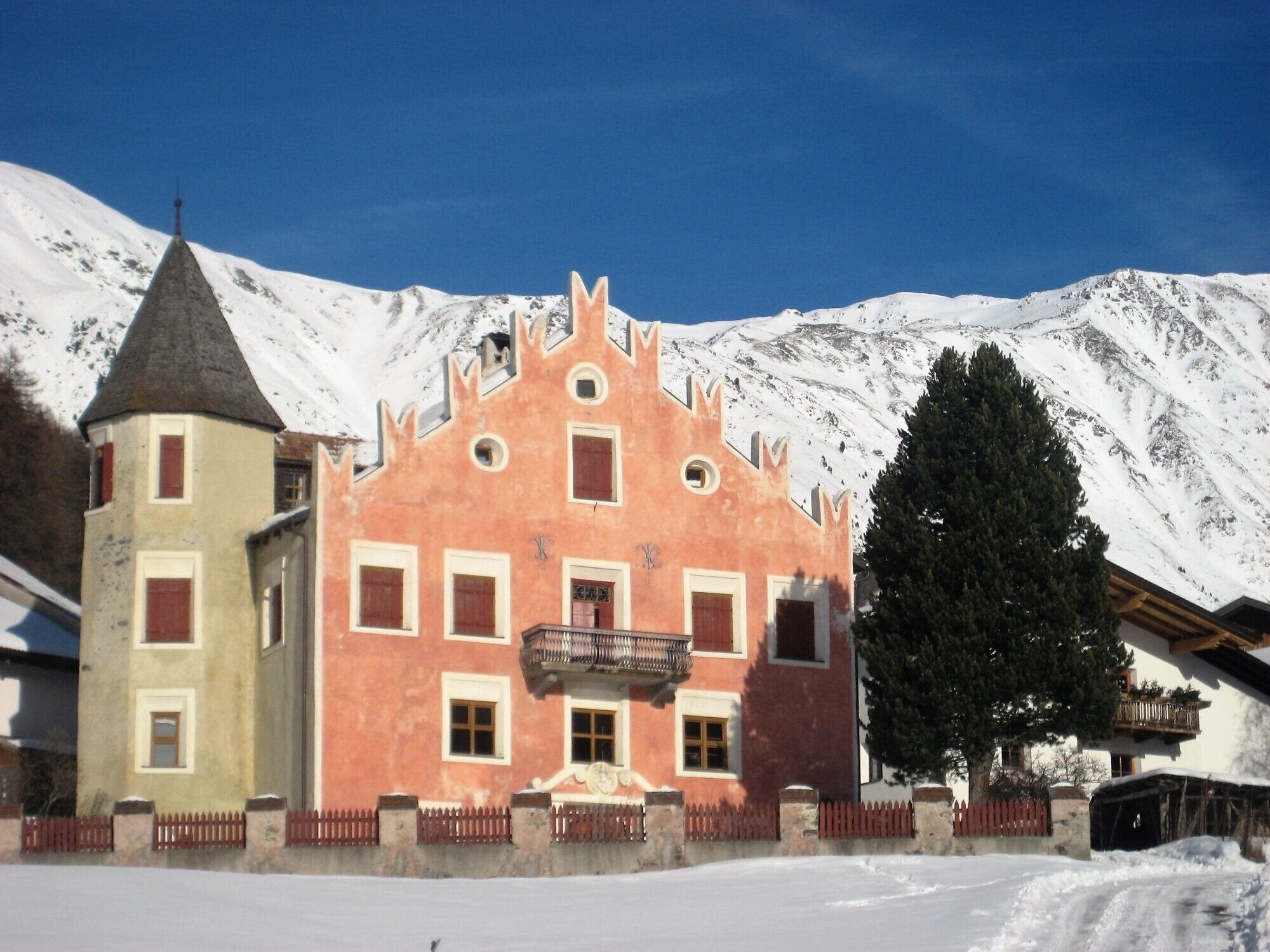 A building with a distinctive pink facade and a tower, surrounded by snow-covered mountains.