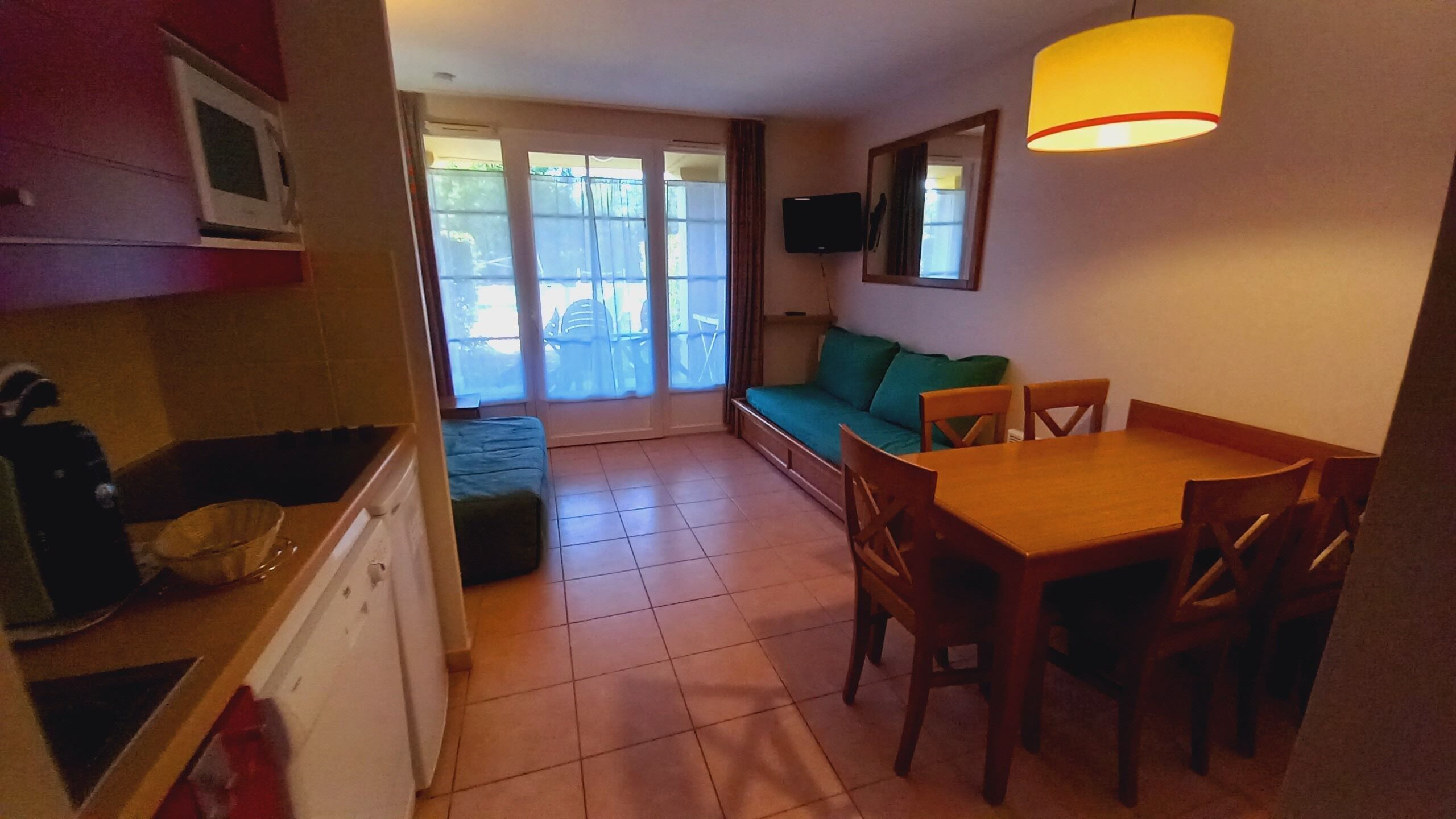 A compact kitchen with a dining area, a sofa, and a TV mounted on the wall.