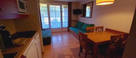 A compact kitchen with a dining area, a sofa, and a TV mounted on the wall.