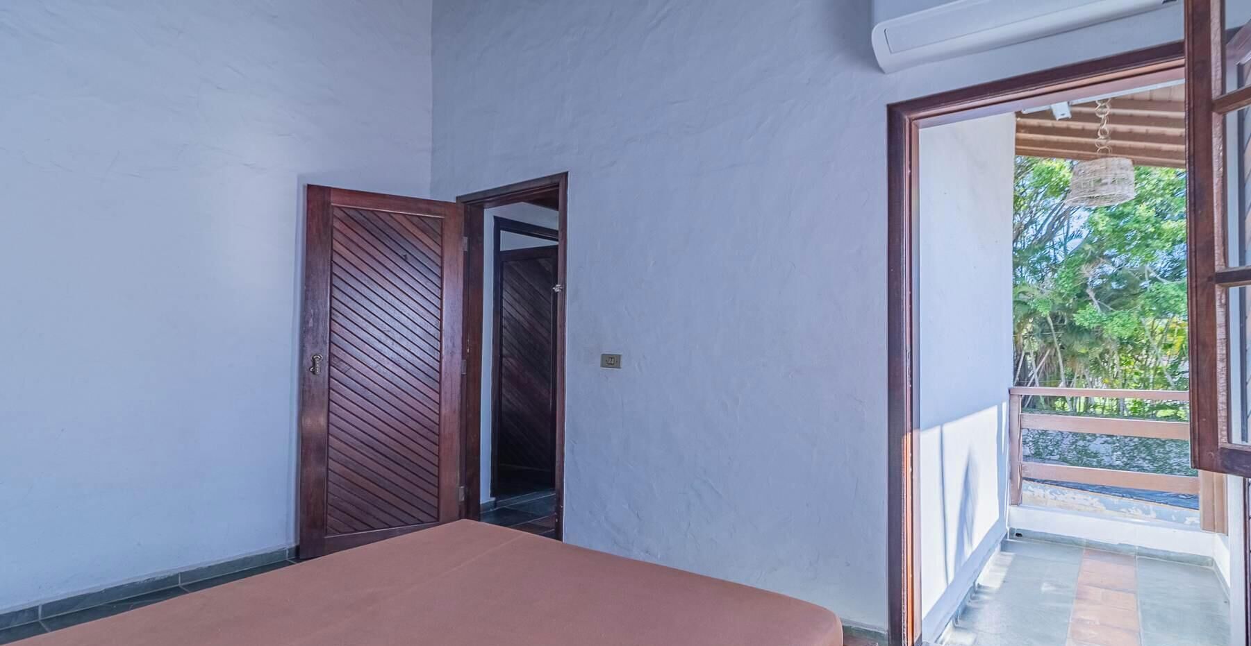Une chambre avec un lit, une porte donnant sur un balcon et une vue sur la verdure.