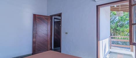 Una habitación con una cama, una puerta que da a un balcón y vistas al exterior con vegetación.