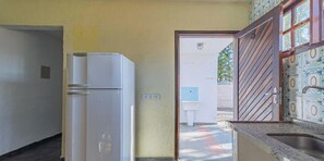 A compact kitchen with a white refrigerator, a sink, and a tiled backsplash. - Casa em Caraguatatuba com Piscina e Churrasqueira (CARAGUATATUBA)