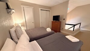 Et hotelværelse med to senge, et fjernsyn, en kommode og en balkon med vindue.