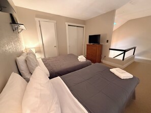 Ein Hotelzimmer mit zwei Betten, einem Fernseher, einem Schminktisch und einem Fenster mit Balkon.