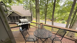 En træterrasse med grill, udendørs siddepladser og udsigt over et boligområde.