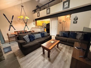 A modern living room with a sofa set, a wooden coffee table, and a dining area with a bench and chairs. - Poconos Ski-In Chalet on Telstar | Loft, Private Deck & Gas Grill (Lake Harmony)