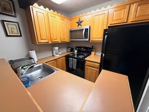 A kitchen with wooden cabinets, a microwave, a stove, a refrigerator, and a coffee maker. - Poconos Ski-In Chalet on Telstar | Loft, Private Deck & Gas Grill (Lake Harmony)