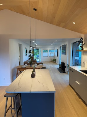 Eine moderne Küche mit Marmorarbeitsplatte, Holzboden und großen Fenstern.