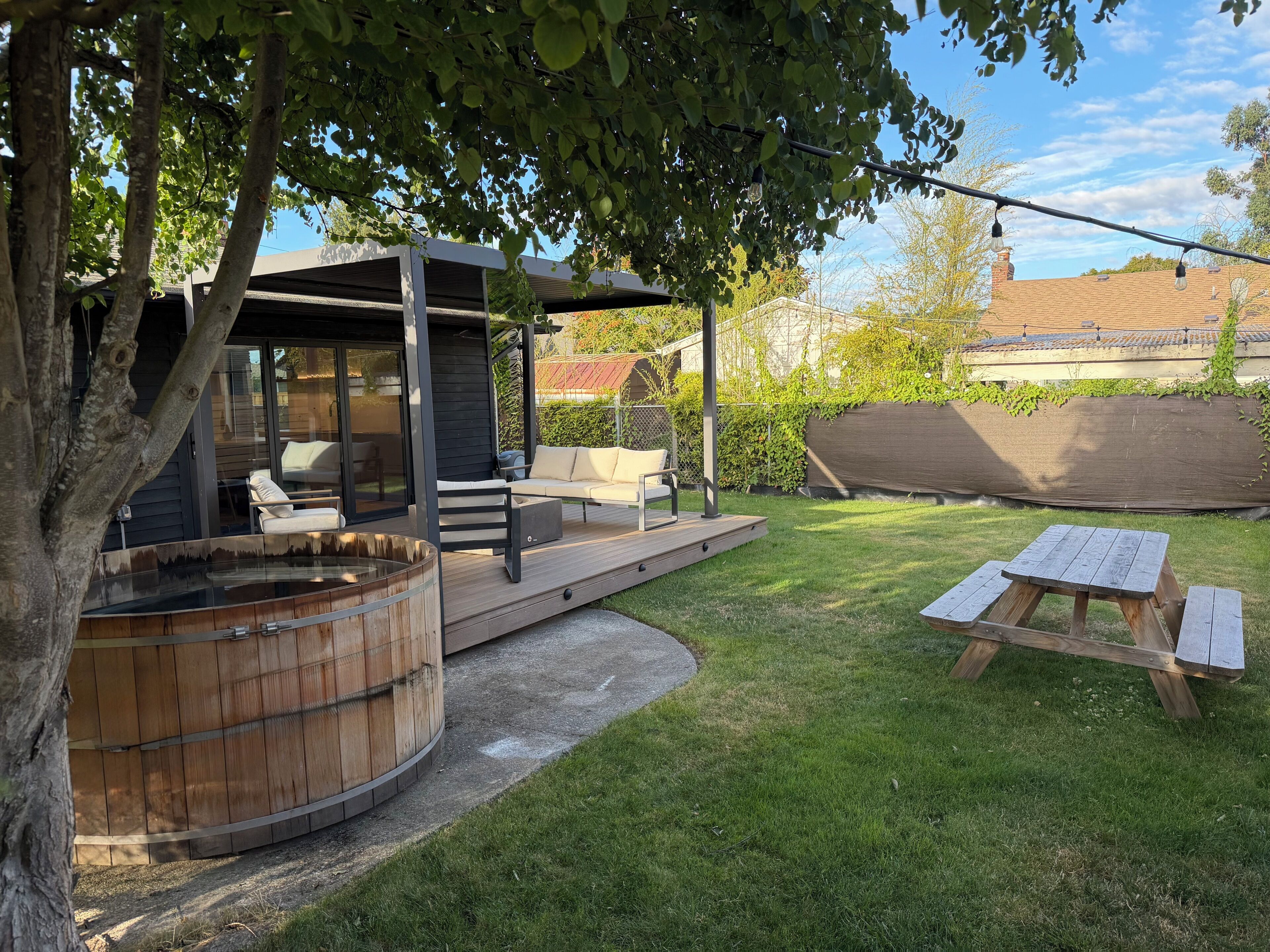 A modern outdoor patio with a hot tub, seating area, and a wooden deck.