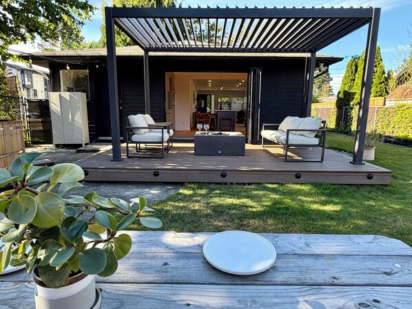 Un patio techado al aire libre con dos sofás, una mesa de centro, una terraza de madera y una planta en maceta.