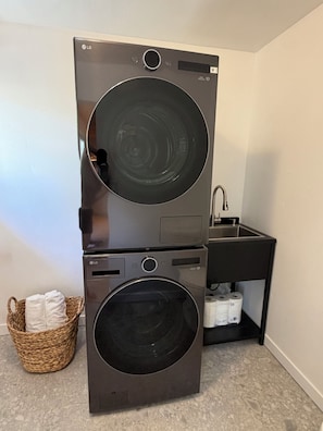 Eine nebeneinander gestellte Waschmaschine und ein Trockner, ein Waschbecken und ein Wäschekorb in einem kleinen Waschraum.
