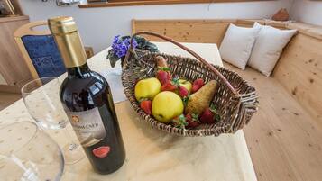 Een fles wijn, een glas en een mand met fruit op een tafel in een kamer met een houten bank en kussens.