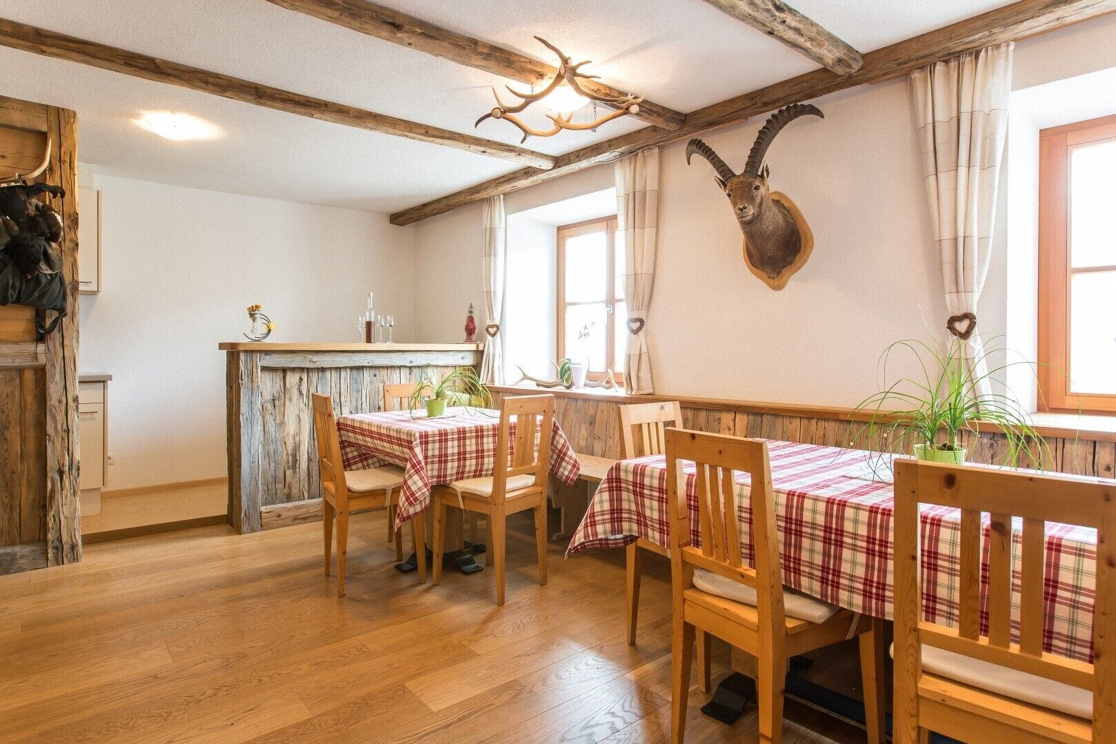 A rustic dining area with wooden tables and chairs, a wooden ceiling, and a mounted animal head on the wall.