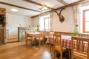 A rustic dining area with wooden tables and chairs, a wooden ceiling, and a mounted animal head on the wall. - Apartment Fürstenburg (Ultimo)