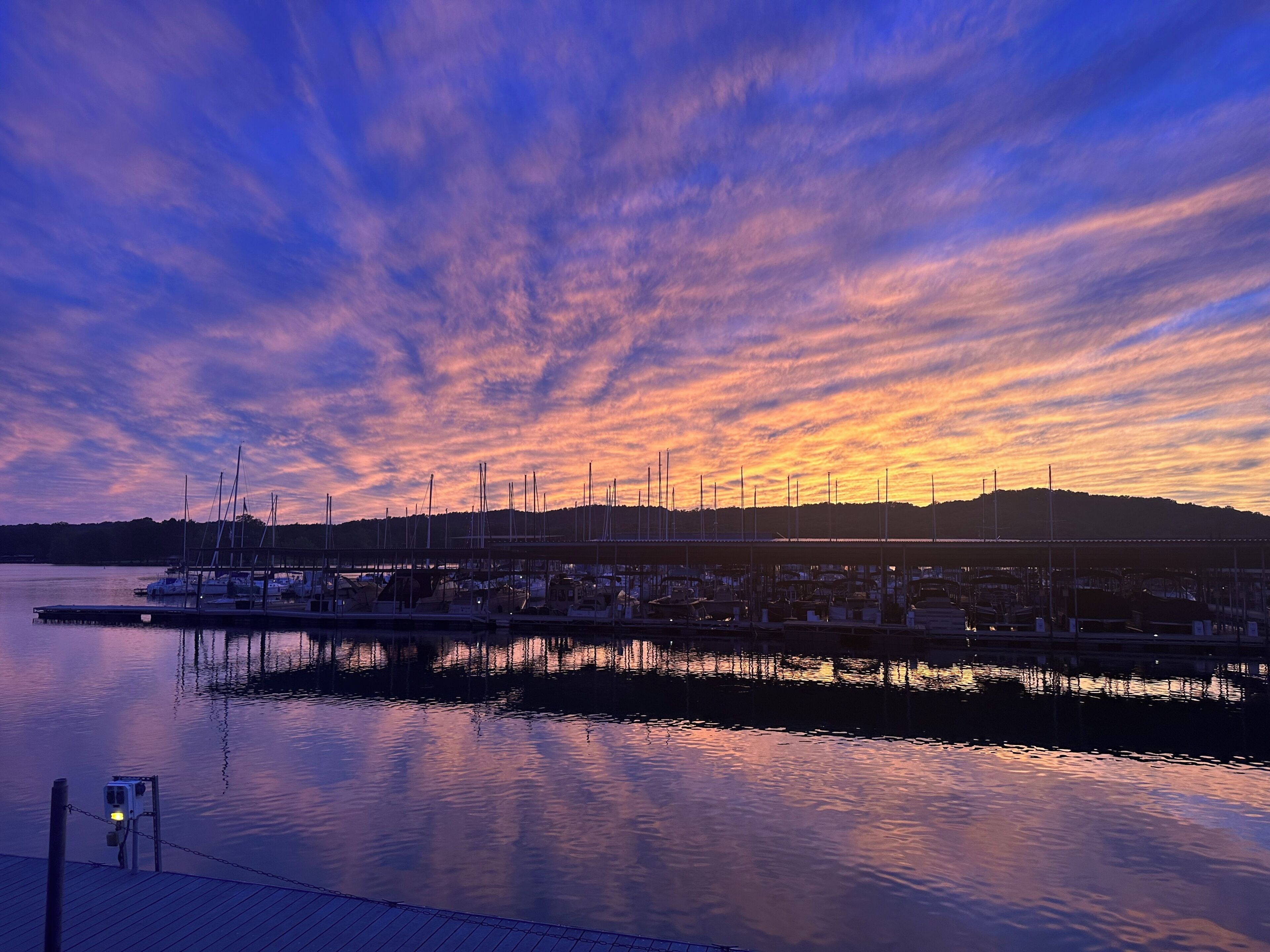 Un port de plaisance avec des bateaux amarrés, une eau calme et un ciel au coucher du soleil.
