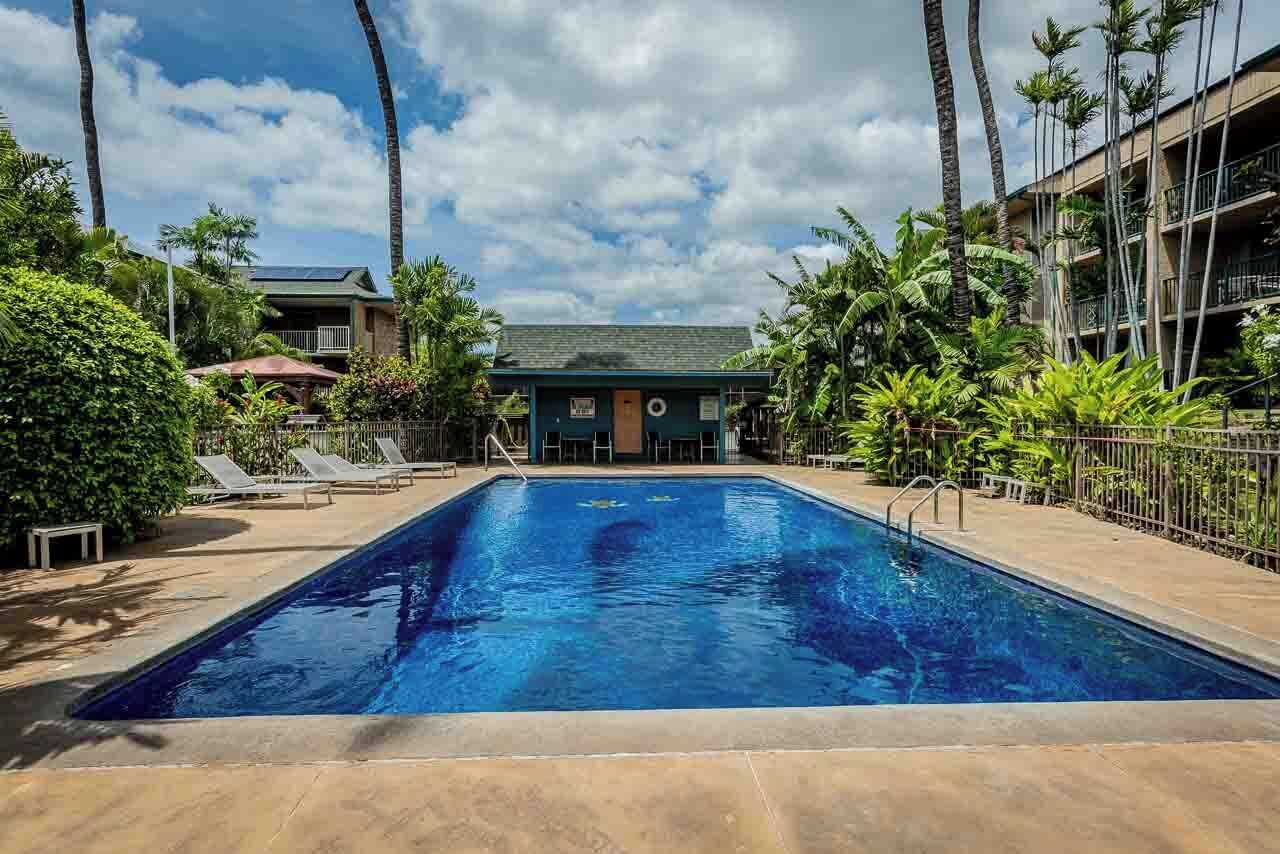 A swimming pool with lounge chairs, surrounded by palm trees and a building with balconies.