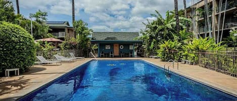 A swimming pool with lounge chairs, surrounded by palm trees and a building with balconies.